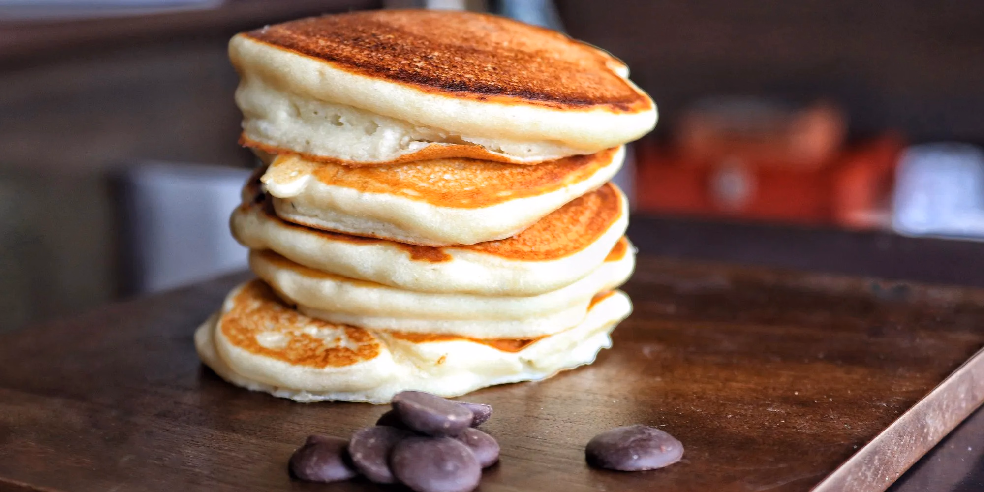 A tall stack of pancakes with syrup running down the side